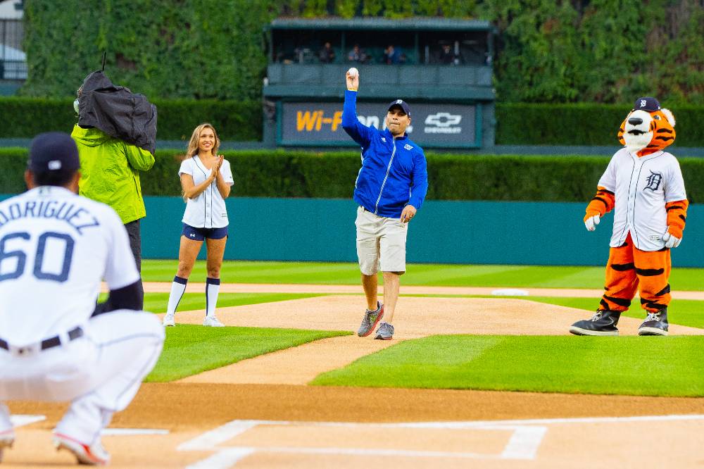 A man throwing the first pitch at the game. The tiger's mascot is there cheering him on.